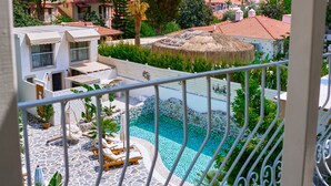 A balcony with a pool, surrounded by greenery and houses with red-tiled roofs.