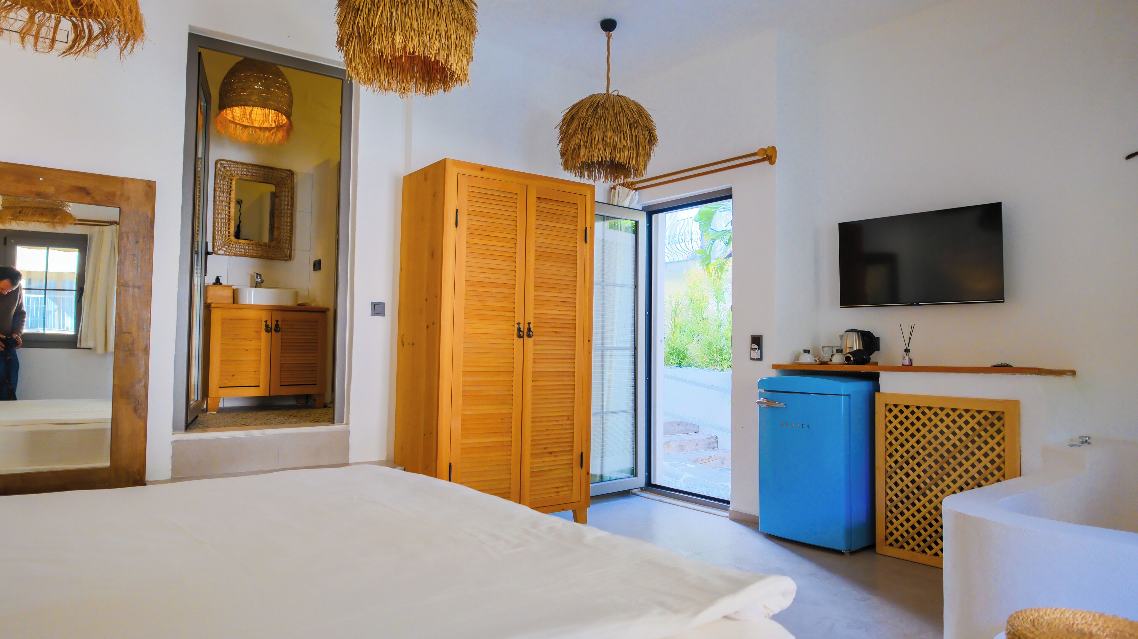 A bedroom with a bed, wooden wardrobe, a television, and a kitchenette.