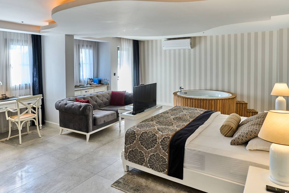 A modern hotel room with a bed, a desk, a television, a small table, and a bathroom with a bathtub.