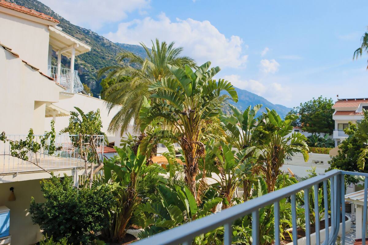 A balcony with a railing, lush greenery, and a mountainous backdrop.