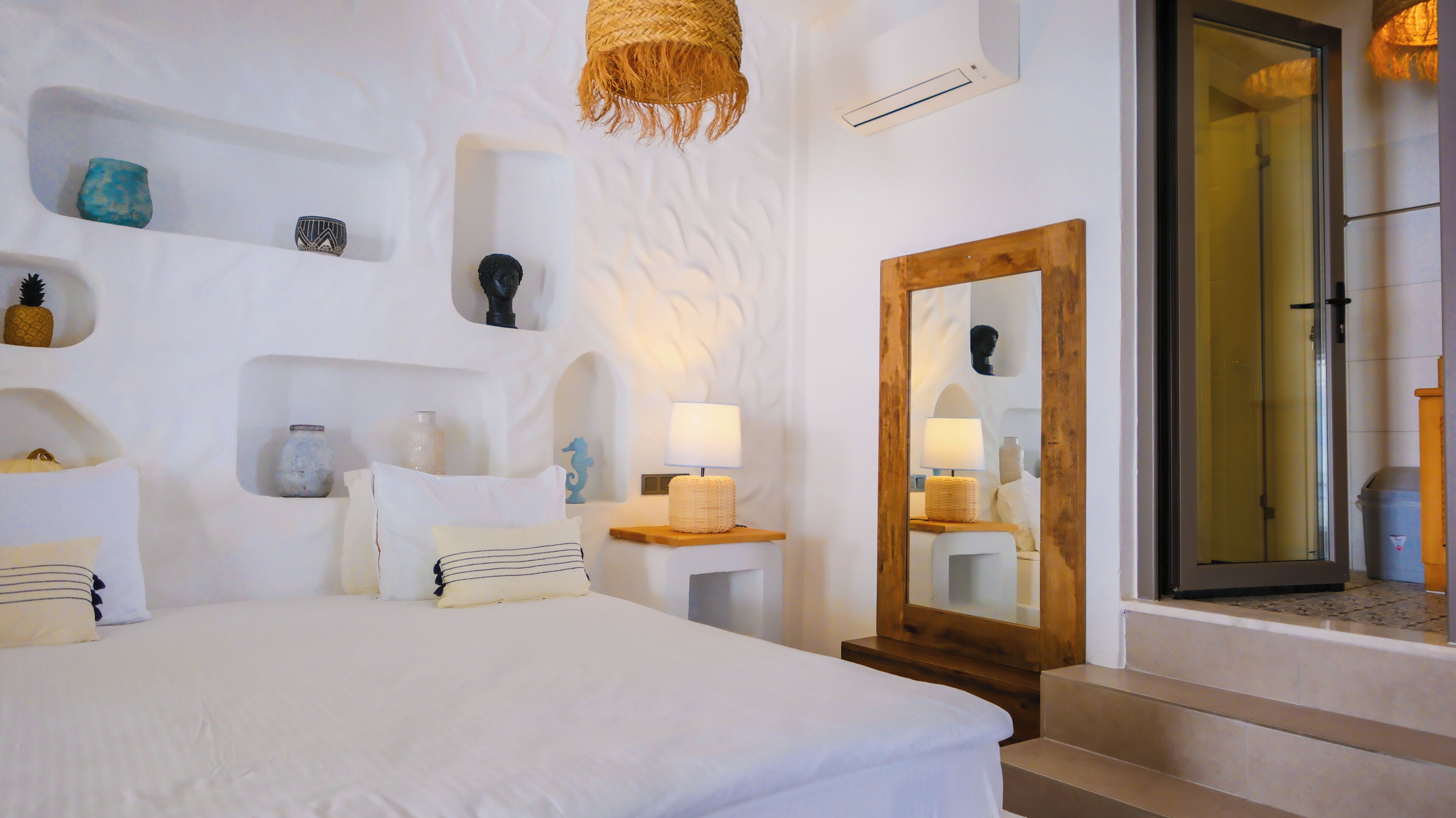 Habitación de hotel con una cama grande, una mesita de noche de madera, un espejo y una repisa con adornos.