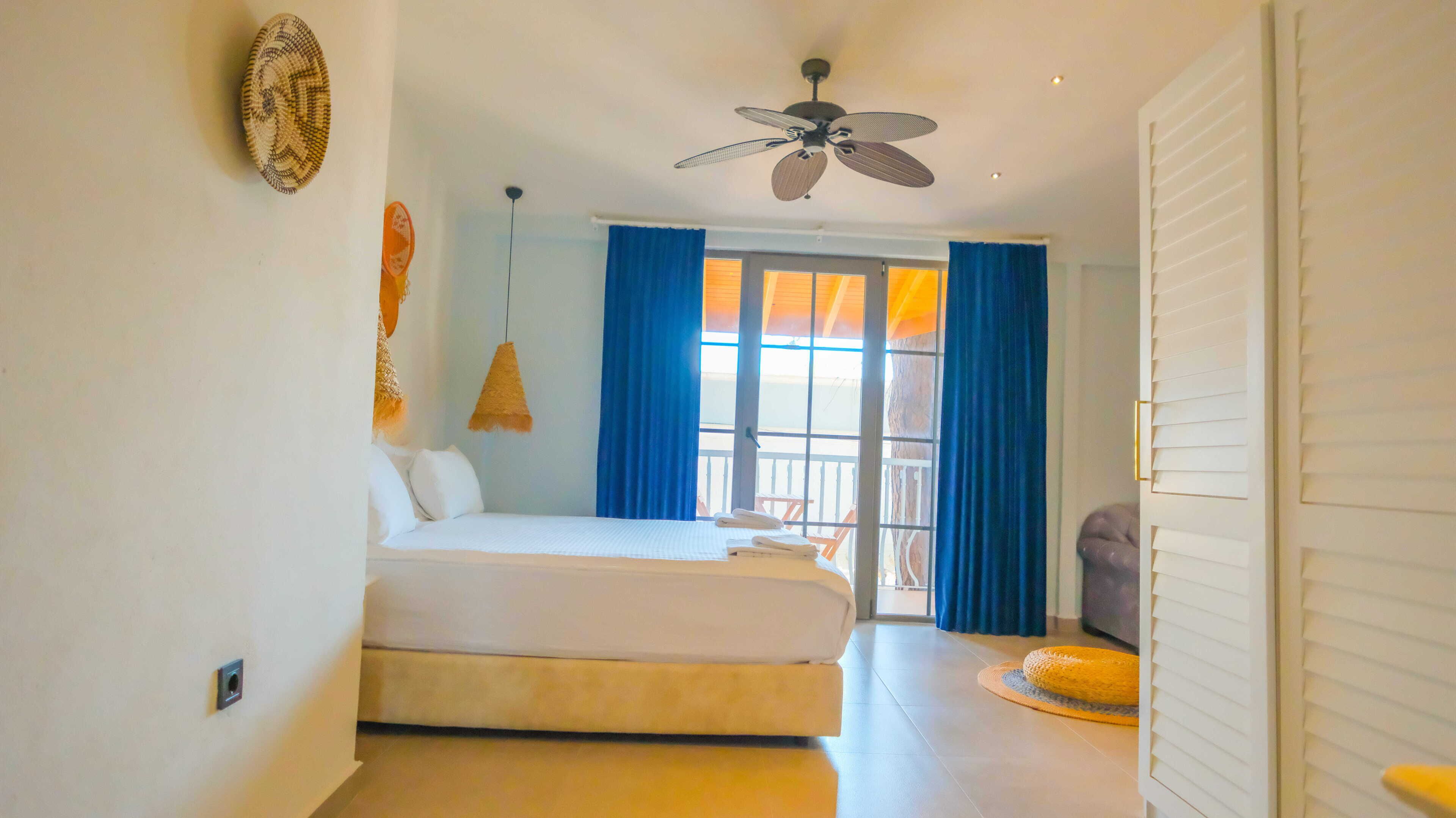 A bedroom with a bed, a ceiling fan, a window with curtains, and a view of the outside.