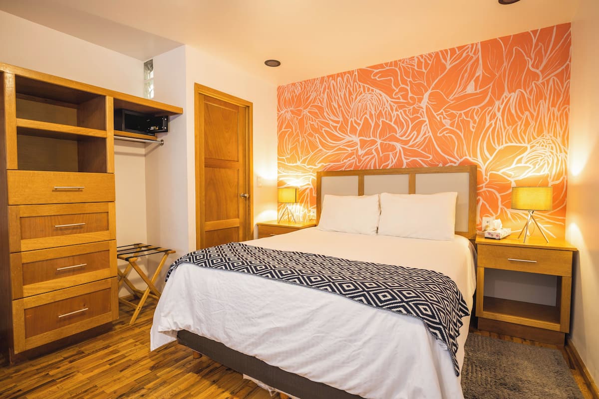 Ein Schlafzimmer mit Bett, Holzschrank und Wand mit Blumenmuster.