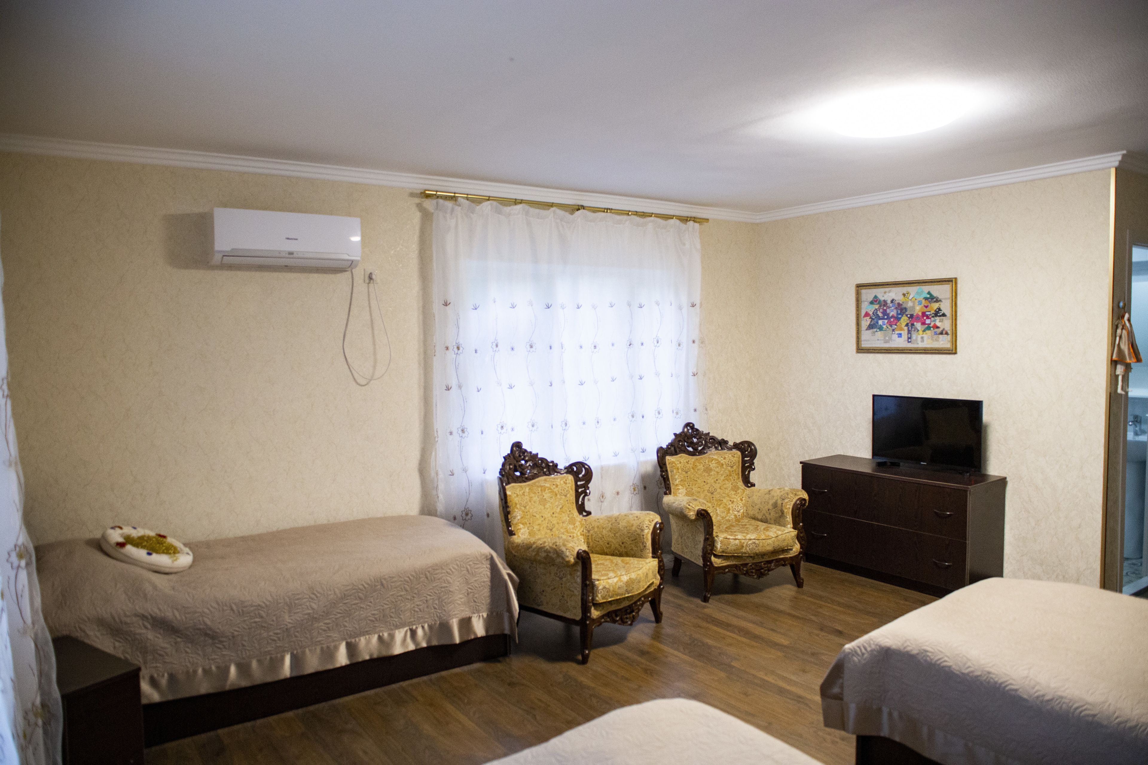 A hotel room with two single beds, a wooden dresser, a television, and two ornate armchairs.