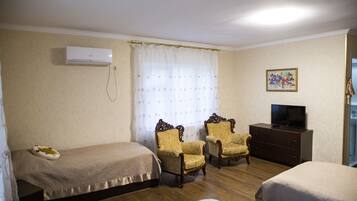 A hotel room with two single beds, a wooden dresser, a television, and two ornate armchairs.