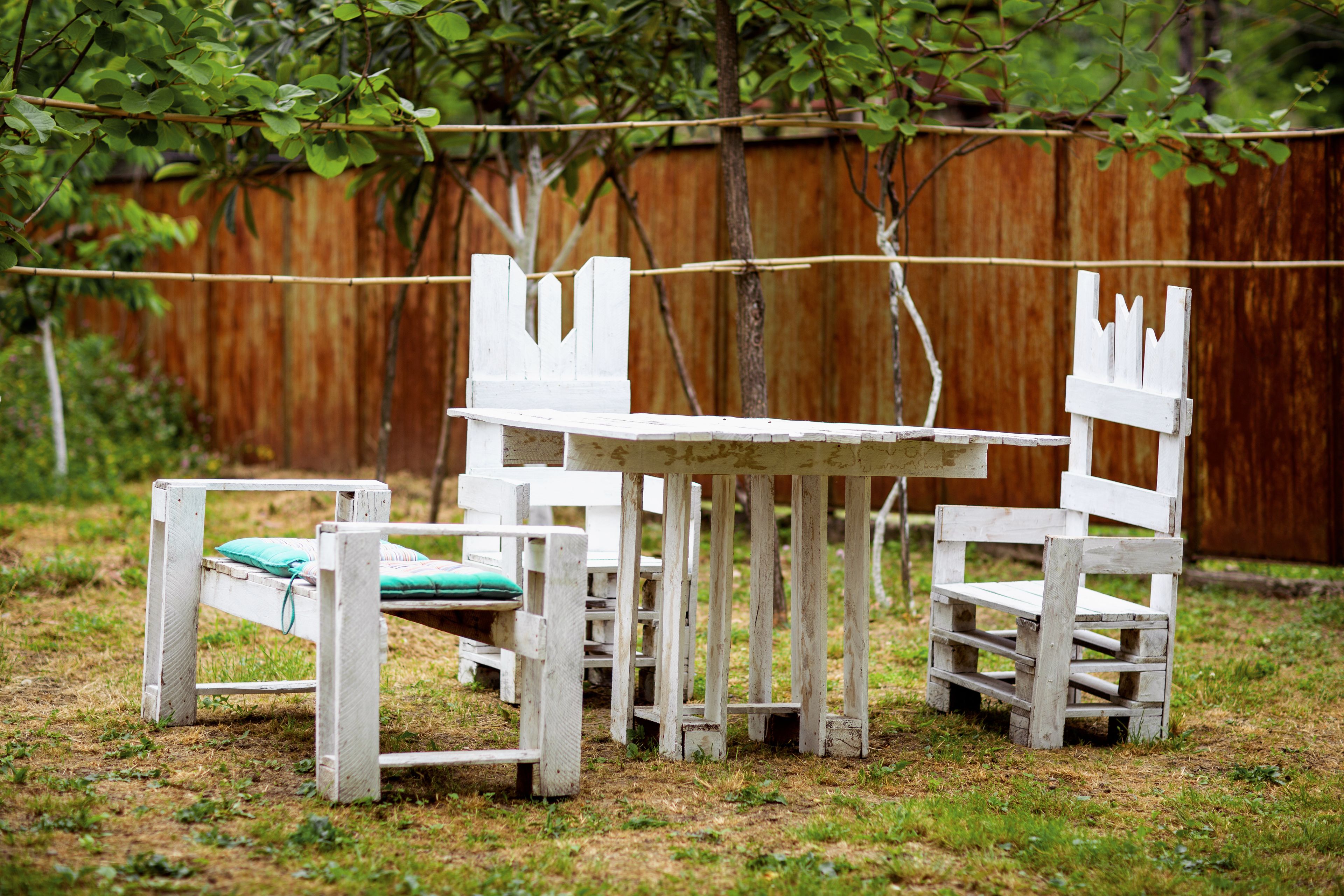 Un espacio de estar al aire libre de estilo rústico con una mesa y sillas de madera, rodeado por una valla de madera y follaje.