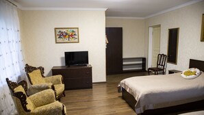 Ein Hotelzimmer mit einem Bett, zwei Sesseln, einem Fernseher, einem Schminktisch und einem Bild an der Wand.