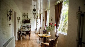 Ein Zimmer mit Holzboden, einem Esstisch mit Stühlen, einem blumigen Ohrensessel, einem Blumentopf und einem Fenster mit Vorhängen.