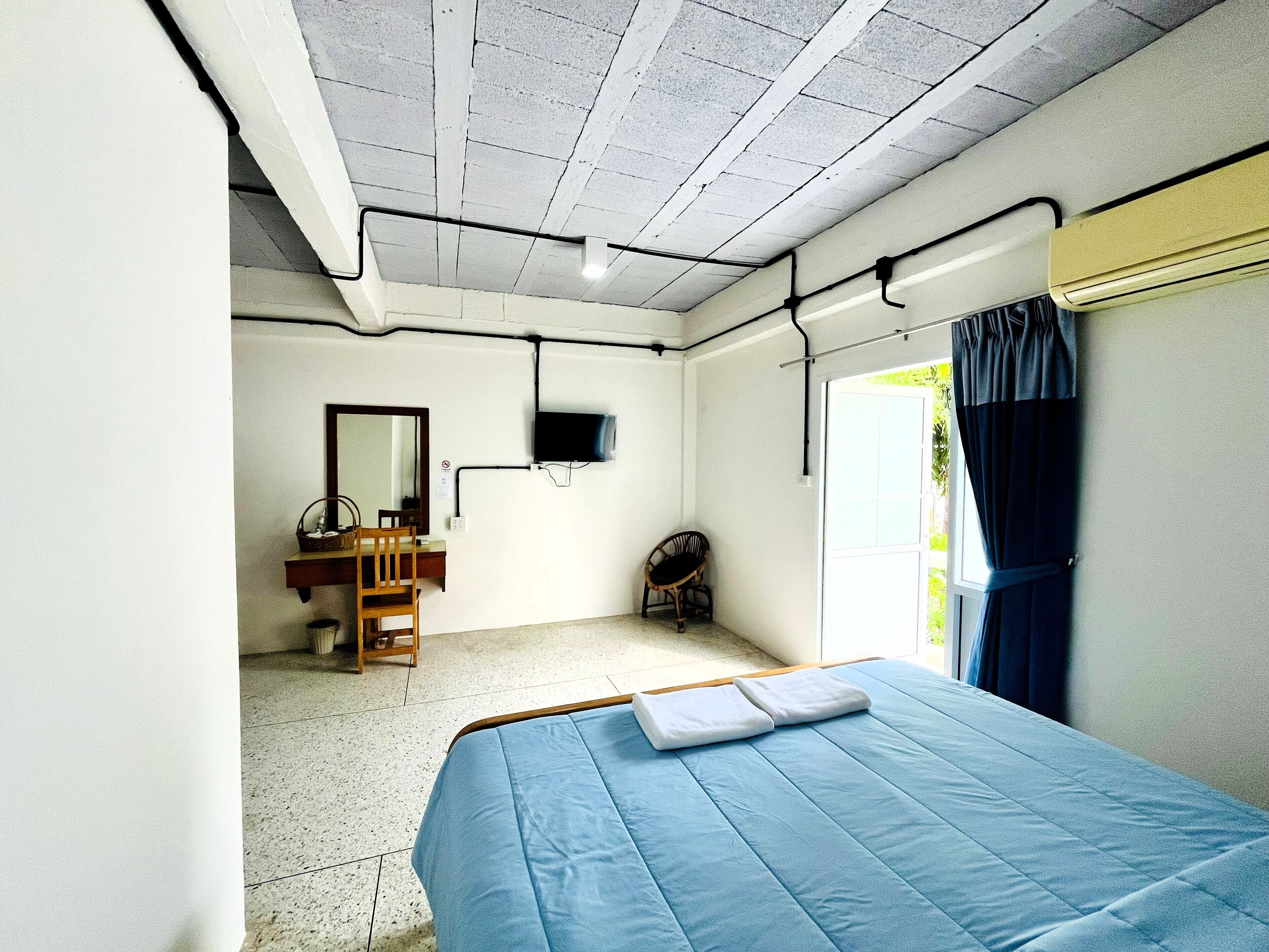 Quarto com cama, escrivaninha, cadeira, televisão e janela com cortinas.
