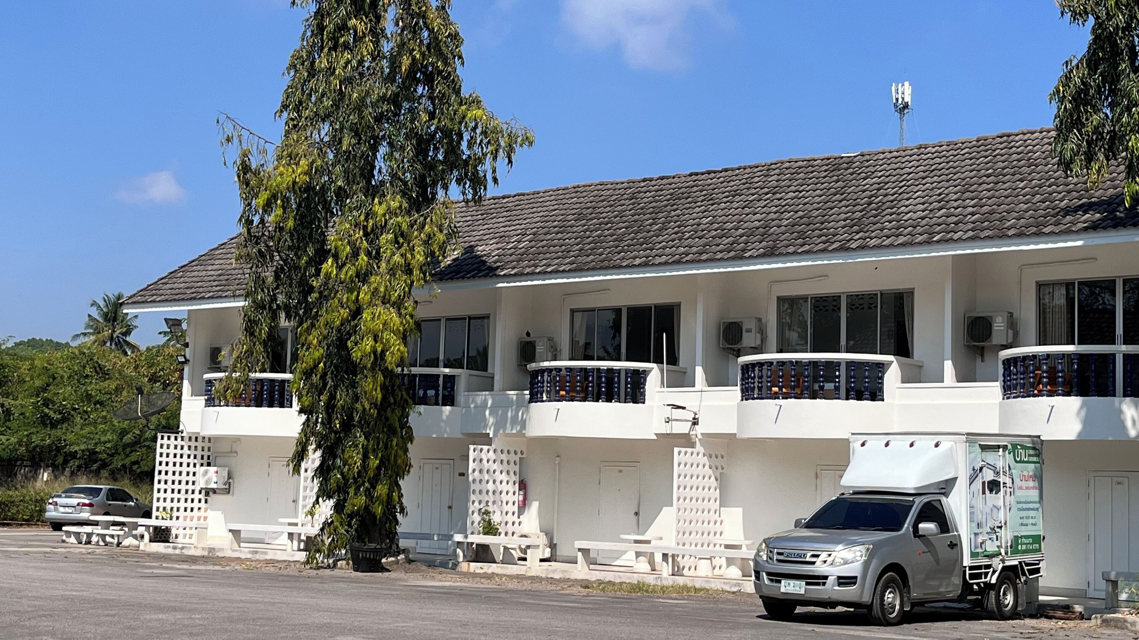 Un edificio de dos plantas con techo de tejas, varios balcones y un camión estacionado al frente.