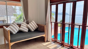 Eine hölzerne Bank mit Kissen und gestreiften Kopfkissen, ein Holzaumschlag und Blick auf einen Swimmingpool.