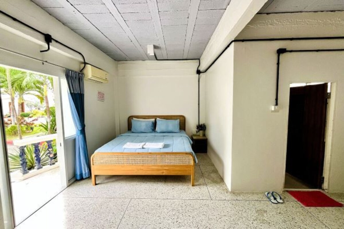 Een slaapkamer met een bed, een nachtkastje, een rode mat en uitzicht op groen buiten.