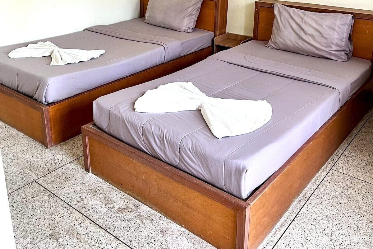 Une chambre avec deux lits en bois, chacun doté d’un matelas et d’un oreiller gris, et une serviette blanche sur chaque lit.