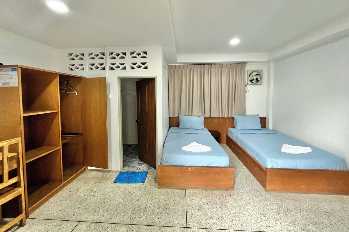 Une petite chambre propre, avec deux lits simples, une armoire et une porte donnant sur la salle de bain.