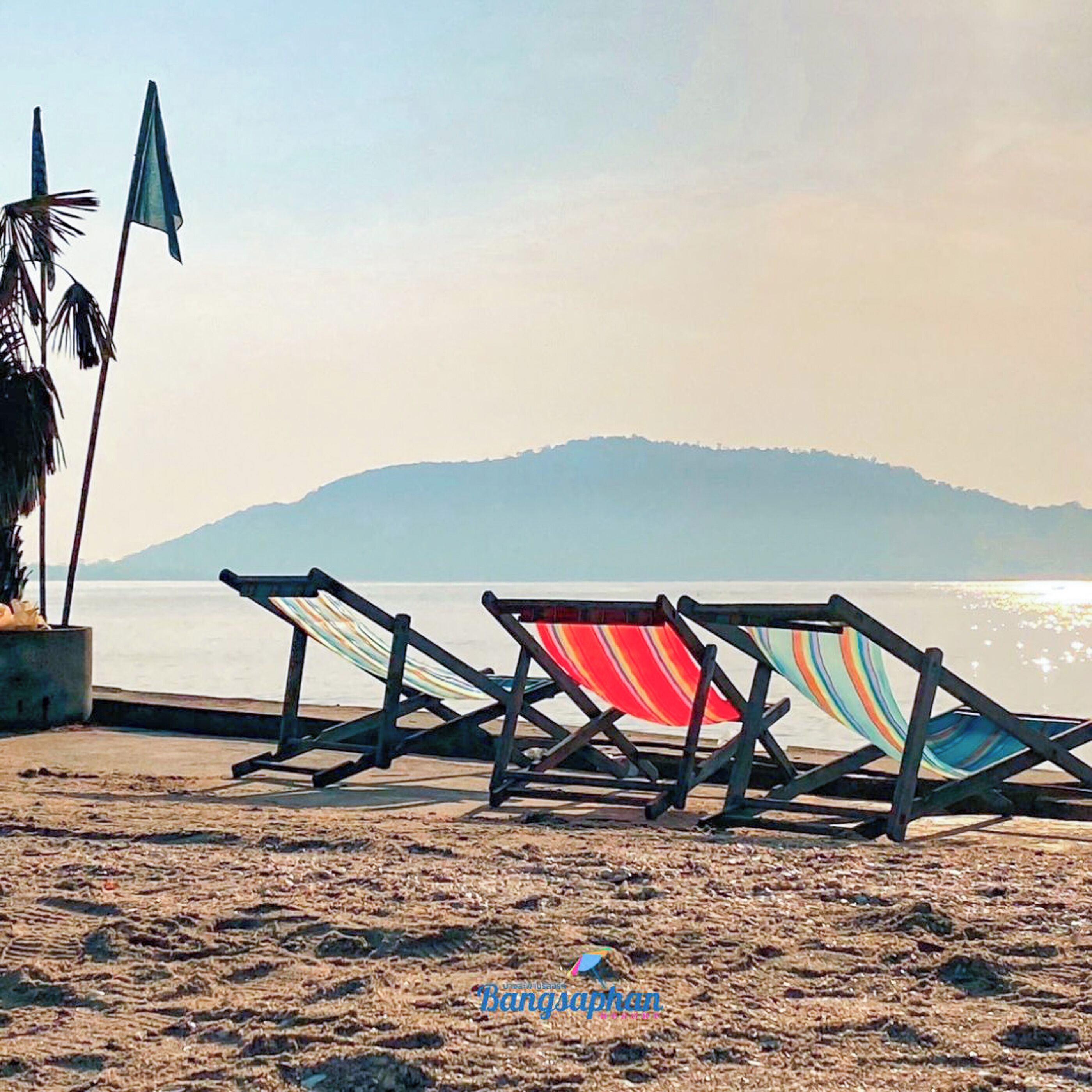 A beach with two striped lounge chairs and a palm tree.