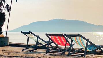 A beach with two striped lounge chairs and a palm tree.
