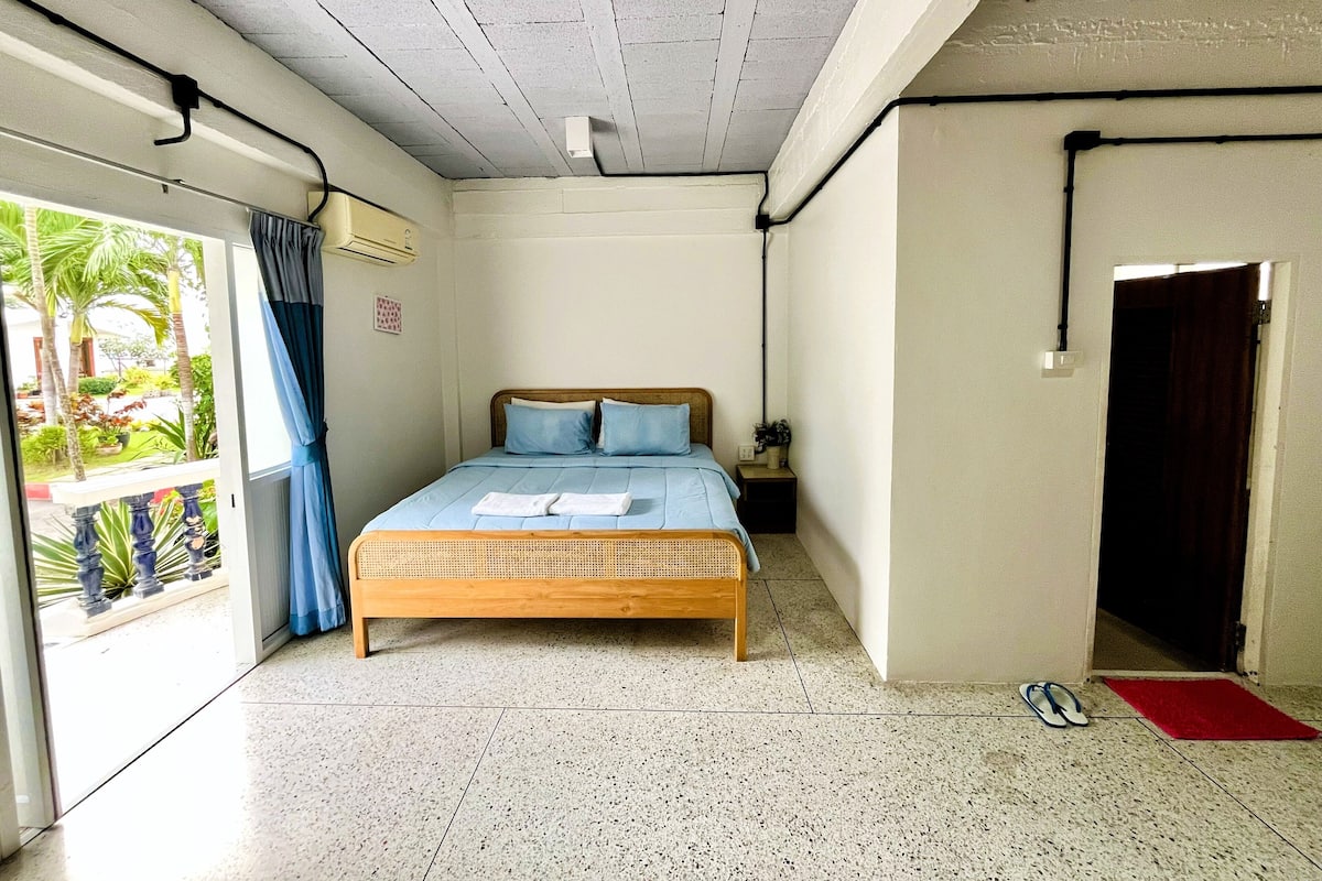 Une chambre à coucher avec un lit, une table de chevet, un tapis rouge et une vue sur un jardin, visible à travers une porte coulissante.