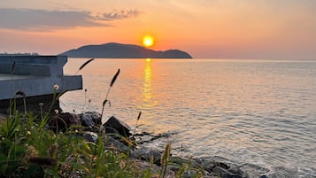 A sunset over a calm body of water with a rocky shoreline and a distant hill.