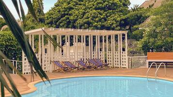 Un área de piscina con un pabellón blanco y sillones de descanso.