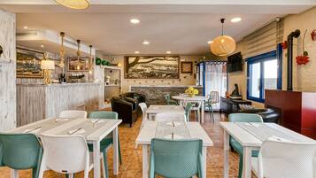 A restaurant with a bar area, seating with green and white chairs, and a stone fireplace.