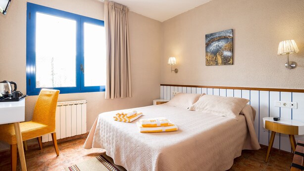 A hotel room with a bed, a desk, a chair, a lamp, and a painting on the wall. - Hostal La Fonda (Cadaqués)