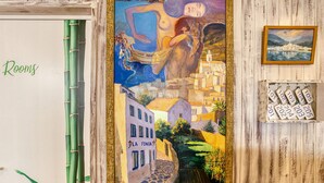 A room with a mural of a woman and a cityscape, a wooden door, and a key rack with room numbers. - Hostal La Fonda (Cadaqués)