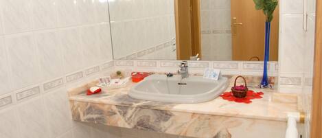 Un baño con lavamanos de mármol, espejo y un florero con flores.