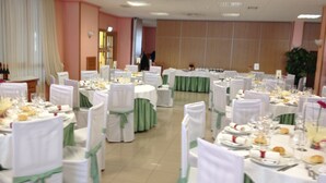 Un salón de banquetes con mesas redondas dispuestas para un evento formal, con manteles blancos y cintas verdes en las sillas.
