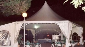 Una gran carpa con techo cónico, rodeada de mesas y sillas, probablemente montada para un evento o reunión.
