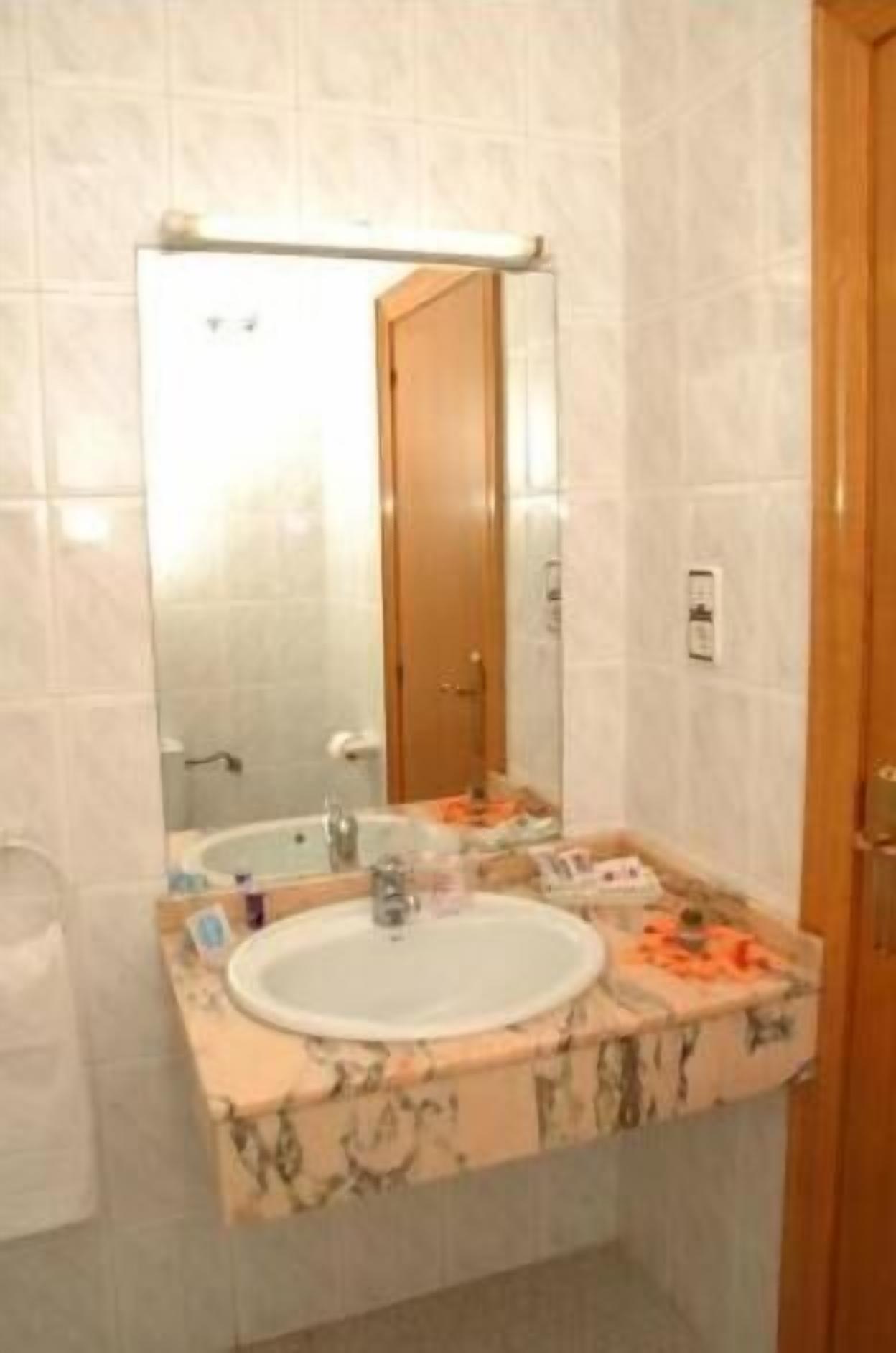 Un baño con lavamanos de mármol, un espejo y una puerta de madera.