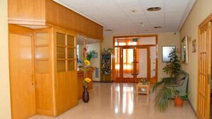 Un vestíbulo de hotel con puertas de madera, una recepción y plantas en macetas.