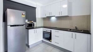 A modern kitchen with white cabinets, a stainless steel refrigerator, a built-in oven, and a black countertop. - Comfort Inn North Brisbane (Carseldine)