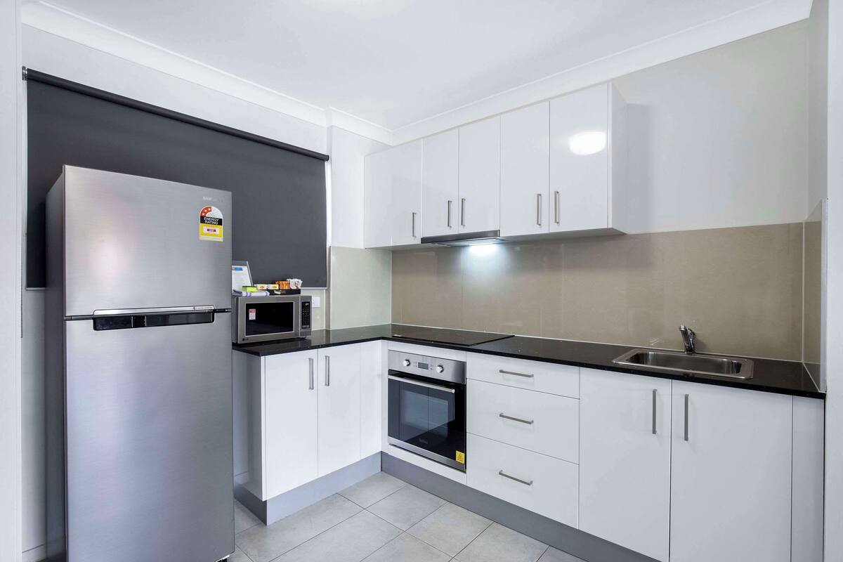 A modern kitchen with white cabinets, a stainless steel refrigerator, a built-in oven, and a black countertop.