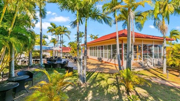 A resort with outdoor seating, palm trees, and a building with large windows. - Comfort Inn North Brisbane (Carseldine)