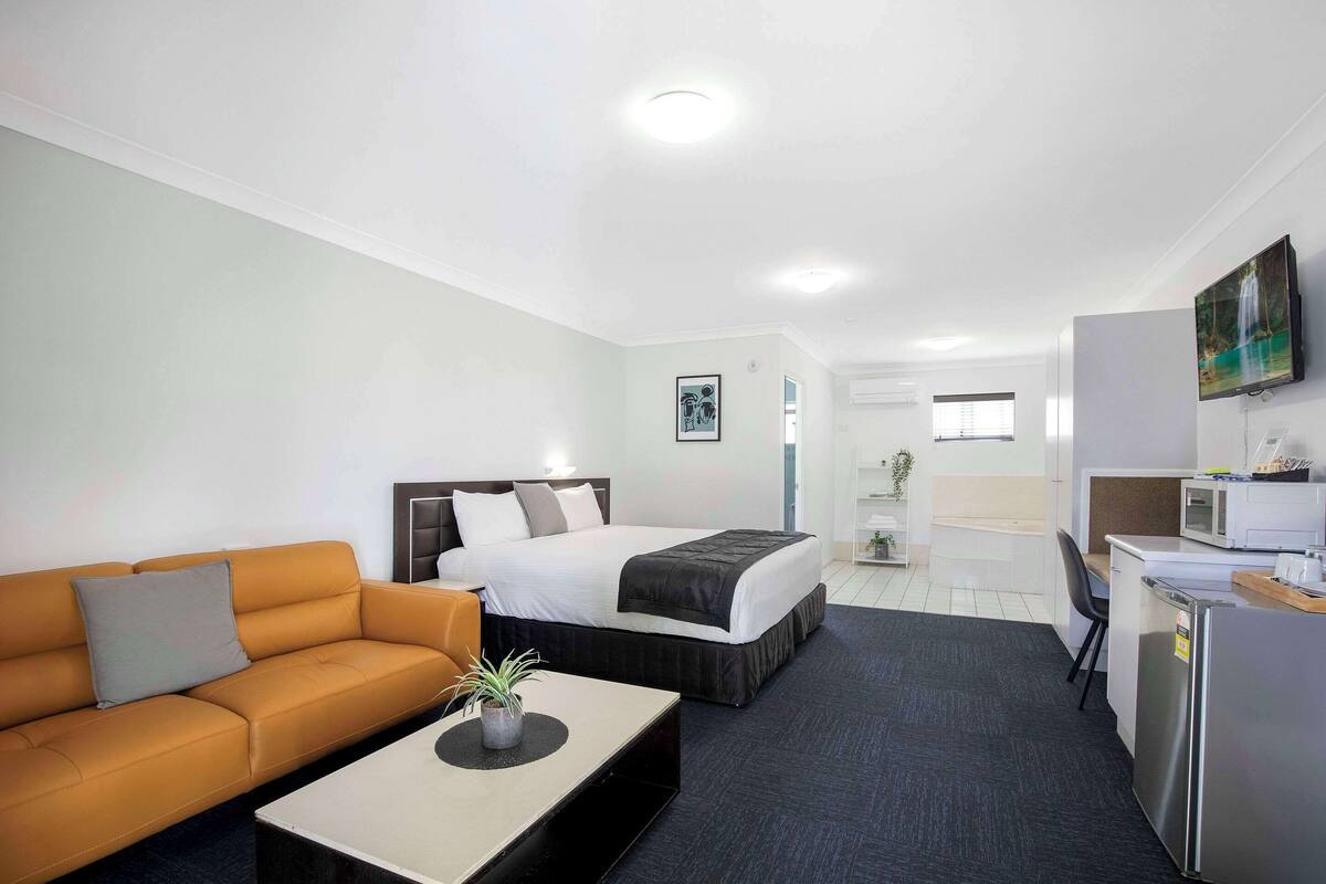 A hotel room with a bed, a sofa, a desk, a refrigerator, and a TV.