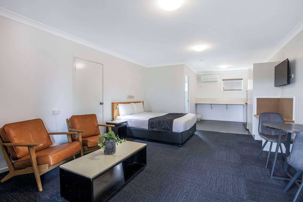 A hotel room with a bed, two chairs, a small table, a TV, and a kitchenette.