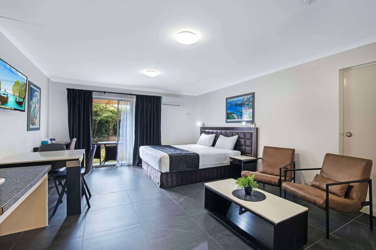 A modern hotel room with a bed, two armchairs, a desk, and a coffee table.