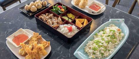 A table with various dishes including rice, vegetables, and fried items, arranged on a marble table.