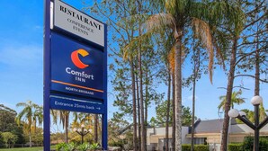 A Comfort Inn sign with a restaurant and conference events notice, located in a landscaped area with trees and a building in the background. - Comfort Inn North Brisbane (Carseldine)