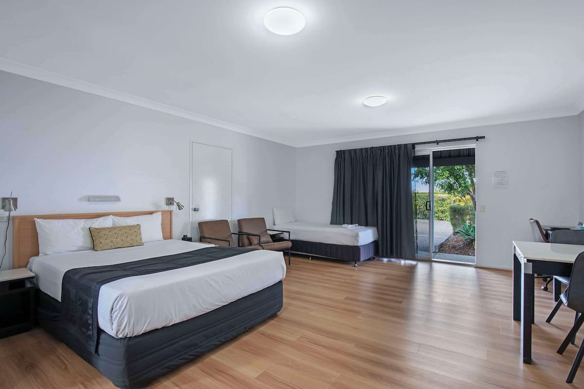 A modern hotel room with a large bed, a desk, and a chair. There is a sliding glass door leading to a balcony.