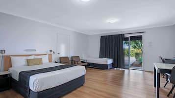 A modern hotel room with a large bed, a desk, and a chair. There is a sliding glass door leading to a balcony.