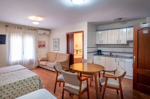 Una habitación compacta con cama, sofá, mesa de comedor con sillas, kitchenette y una puerta con el número 204.