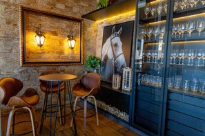 A bar area with a stone wall, two wall-mounted lights, a large framed horse portrait, and a glass display case with wine glasses. - Brii hotel (Araguaina)