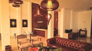 A living room with a brown leather sofa, two armchairs, a coffee table, and a patterned rug. There are framed pictures on the wall and a decorative wall panel. - Brii hotel (Araguaina)