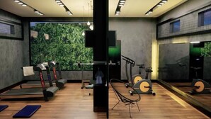 A modern gym with exercise equipment, a wooden floor, and a large window with a view of greenery. - Brii hotel (Araguaina)