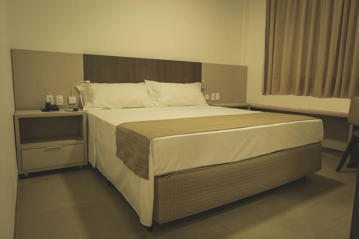 A hotel room with a large bed, a bedside table, a desk, and a chair.