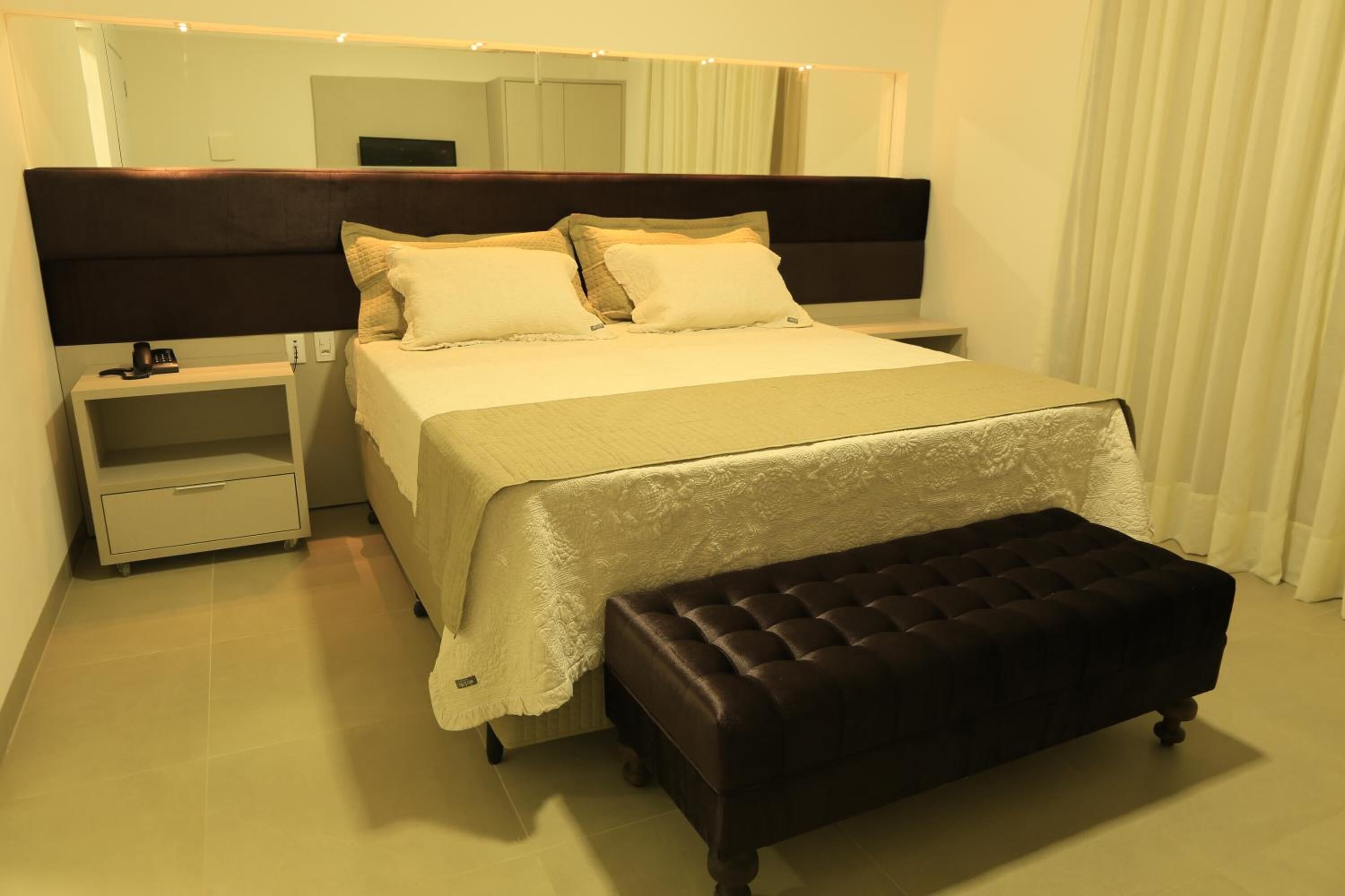 A neatly arranged bedroom with a bed, bedside tables, a bench, and a large mirror.