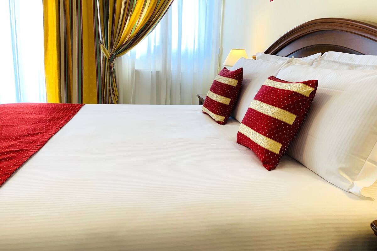 A hotel room with a neatly made bed, two pillows with red and gold patterns, and a wall with a sign that reads "Wonderful Way".