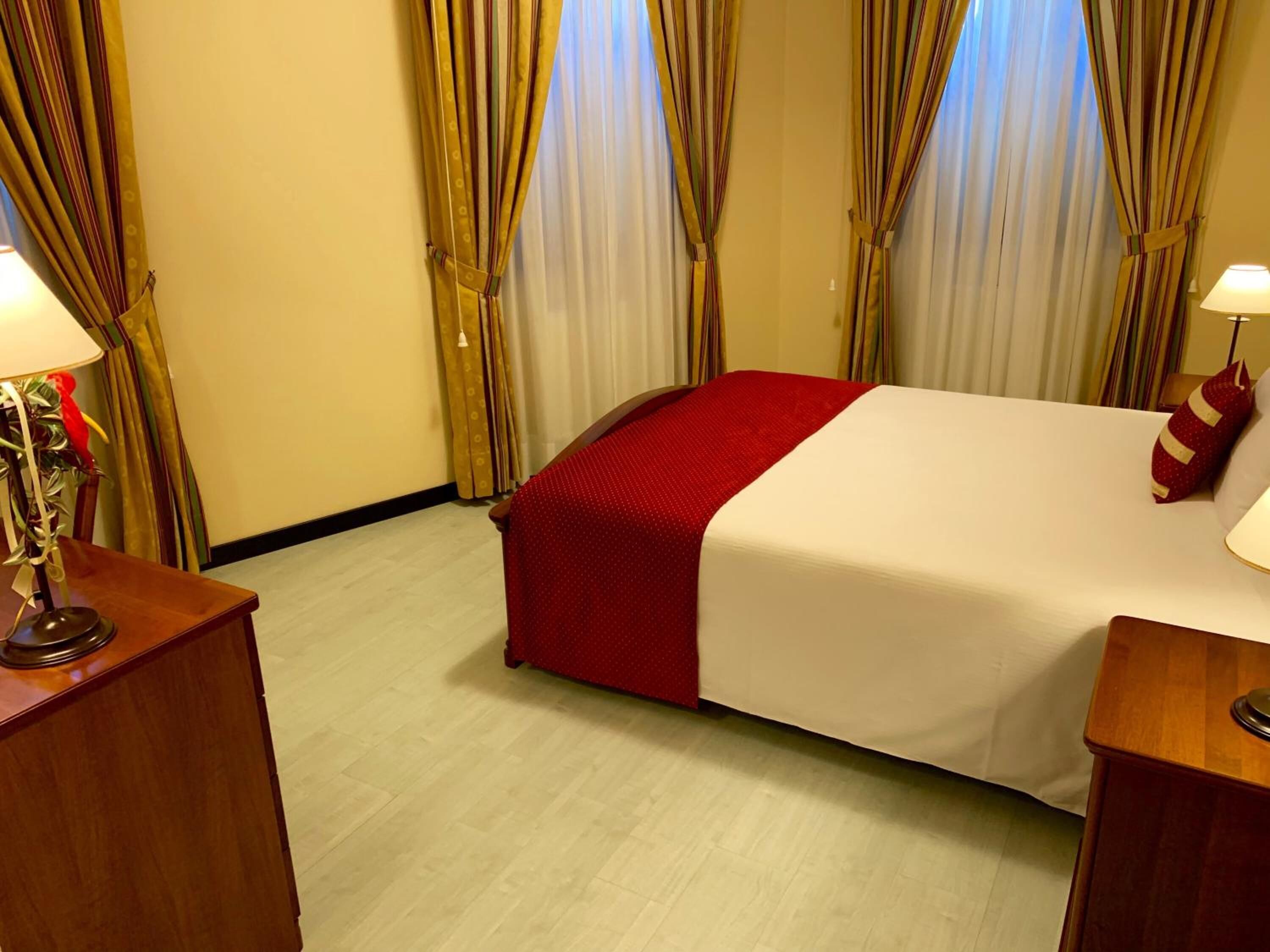 Een hotelkamer met een bed, gordijnen, een lamp en een nachtkastje van hout.