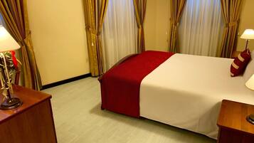 Een hotelkamer met een bed, gordijnen, een lamp en een nachtkastje van hout.